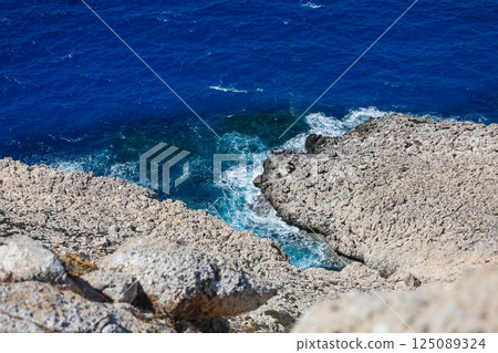 Crystal-clear waves caress the rugged shores of Ayia Napa in Larnaka, Cyprus under the bright sun 125089324