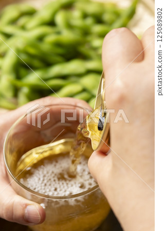 用手將罐裝啤酒倒入玻璃杯中 用手將罐裝啤酒倒入玻璃杯中 125089802