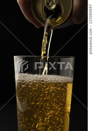 Pouring canned beer into a glass on a black background Pouring canned beer into a glass on a black background 125089847
