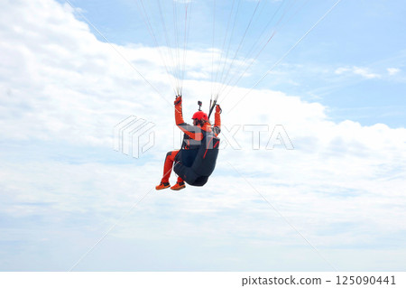Sestri Levante, Italy - 12 April 2025. Paraglider with camera on helmet fly against sky Sport and health. Nature and man. Summer and holiday concept. 125090441