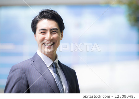 Close-up of a young male office worker looking up to the future and goals with a smile in front of an urban building against the blue sky 125090483