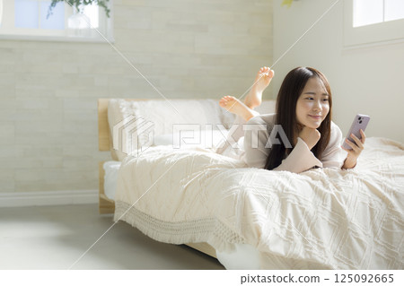 一名婦女在床上的看一個智能手機 一名婦女在床上的看一個智能手機 125092665