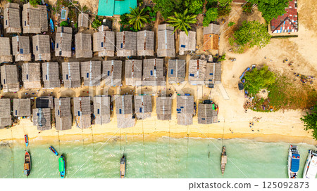 A stunning aerial view of a tropical beach village with rows of small huts along the coastline, A stunning aerial view of a tropical beach village with rows of small huts along the coastline, 125092873