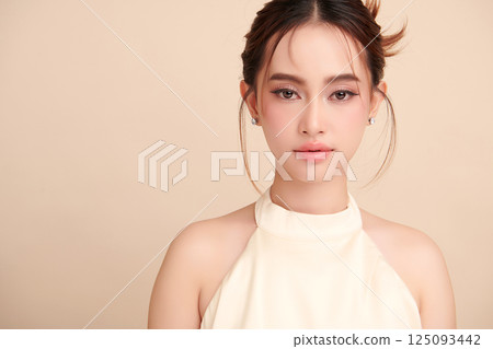 A beautiful young Asian woman with clean, fresh skin against a beige background. Skincare, facial treatment, cosmetology, beauty, and spa. An elegant portrait of an Asian woman. 125093442