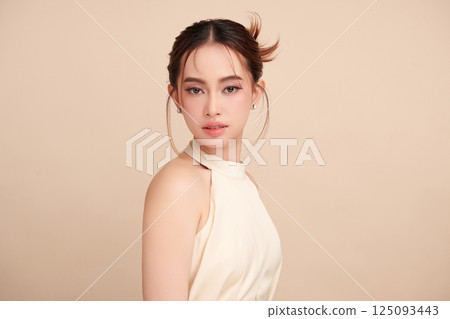 A beautiful young Asian woman with clean, fresh skin against a beige background. Skincare, facial treatment, cosmetology, beauty, and spa. An elegant portrait of an Asian woman. 125093443