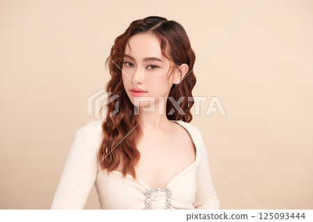 A beautiful young Asian woman with clean, fresh skin against a beige background. Skincare, facial treatment, cosmetology, beauty, and spa. An elegant portrait of an Asian woman. 125093444