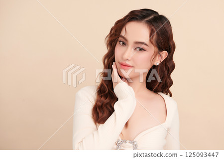 A beautiful young Asian woman with clean, fresh skin against a beige background. Skincare, facial treatment, cosmetology, beauty, and spa. An elegant portrait of an Asian woman. 125093447
