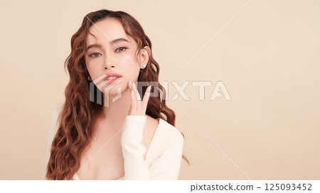 A beautiful young Asian woman with clean, fresh skin against a beige background. Skincare, facial treatment, cosmetology, beauty, and spa. An elegant portrait of an Asian woman. 125093452