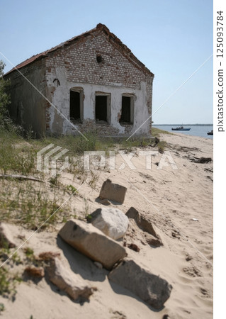 Abandoned house on sandy beach with scattered rocks and serene waters 125093784