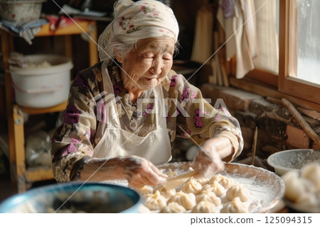 An elderly woman skillfully makes traditional dumplings, her hands carefully shaping the dough in a rustic kitchen setting 125094315