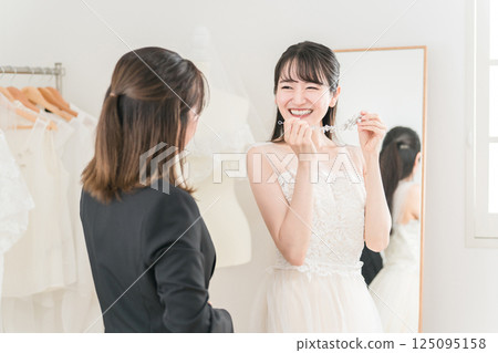 A bride in a wedding dress choosing a head dress and a wedding planner woman A bride in a wedding dress choosing a head dress and a wedding planner woman 125095158