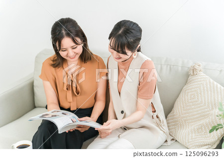 Asian woman looking at a fashion magazine or catalog while chatting with her female friend 125096293