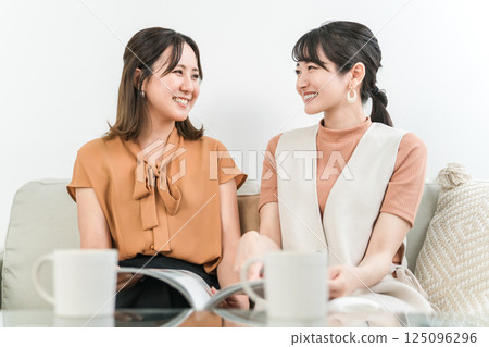 Asian woman looking at a fashion magazine or catalog while chatting with her female friend Asian woman looking at a fashion magazine or catalog while chatting with her female friend 125096296