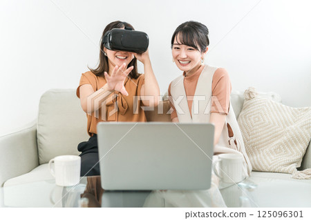 Asian woman wearing VR goggles playing games, experiencing virtual reality, and operating the device (AR, MR) 125096301