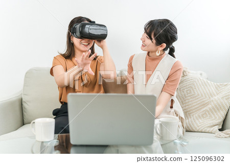 Asian woman wearing VR goggles playing games, experiencing virtual reality, and operating the device (AR, MR) 125096302