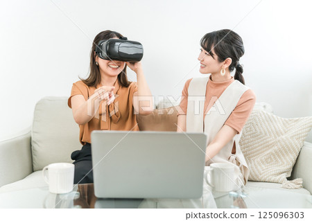Asian woman wearing VR goggles playing games, experiencing virtual reality, and operating the device (AR, MR) 125096303