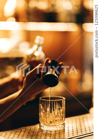 Barista pouring vodka into glass from measuring cup Barista pouring vodka into glass from measuring cup 125096625