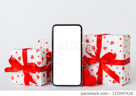 mobile phone with blank screen on colored background with hearts, calendar and gift box, valentine day concept perspertive view flat lay 125097428