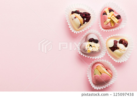 chocolate sweets in the form of a heart with fruits and nuts on a colored background. top view with space for text, holiday concept chocolate sweets in the form of a heart with fruits and nuts on a colored background. top view with space for text, holiday concept 125097438