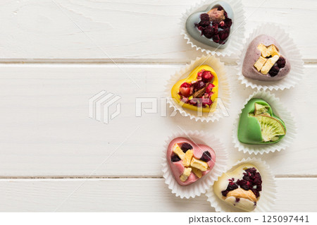 chocolate sweets in the form of a heart with fruits and nuts on a colored background. top view with space for text, holiday concept chocolate sweets in the form of a heart with fruits and nuts on a colored background. top view with space for text, holiday concept 125097441