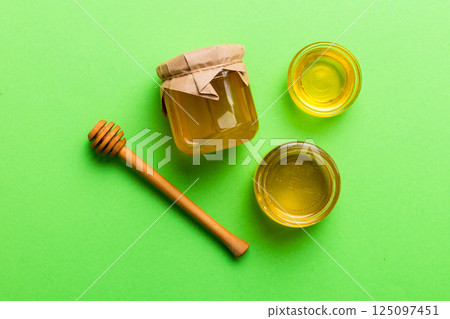 Glass jar of honey with wooden drizzler on colored background. Honey pot and dipper high above. Top view copy space 125097451