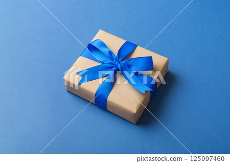 Wrapped christmas or other holiday handmade present in craft paper with colored ribbon. Present box, decoration of gift on table, top view with copy space 125097460