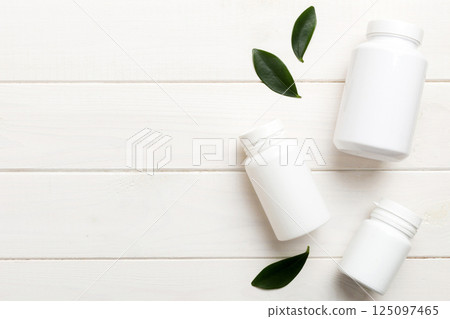 supplement pills with medicine bottle health care and medical top view. Vitamin tablets. Top view mockup bottle for pills and vitamins with green leaves, natural organic bio supplement, copy space 125097465
