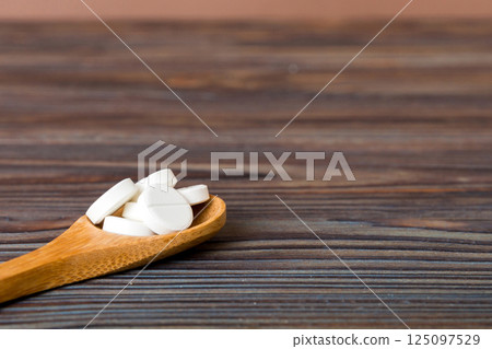 Heap of white pills on colored background. Tablets scattered on a table. Pile of red soft gelatin capsule. Vitamins and dietary supplements concept Heap of white pills on colored background. Tablets scattered on a table. Pile of red soft gelatin capsule. Vitamins and dietary supplements concept 125097529