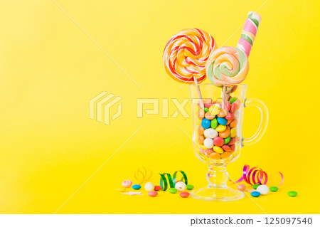 Colorful candies in cup on table on light background background. Large swirled lollipops. Creative concept of a jar full of delicious sweets from the candy store Colorful candies in cup on table on light background background. Large swirled lollipops. Creative concept of a jar full of delicious sweets from the candy store 125097540