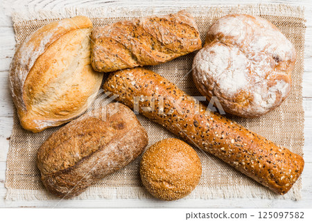 Assortment of freshly baked bread with napkin on rustic table top view. Healthy unleavened bread. French bread Assortment of freshly baked bread with napkin on rustic table top view. Healthy unleavened bread. French bread 125097582