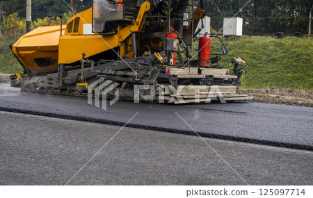 Asphalt paver machine laying fresh asphalt on road construction site. Asphalt paver machine laying fresh asphalt on road construction site. 125097714