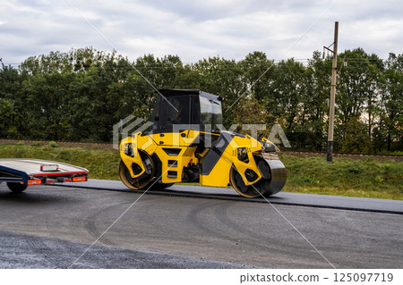 Heavy asphalt road roller that press new hot asphalt on the roadway on a road construction site on a street. 125097719