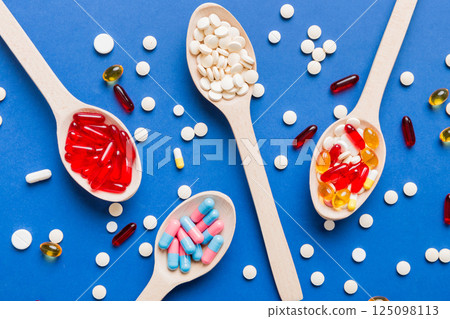 Vitamin capsules in a spoon on a colored background. Pills served as a healthy meal. Red soft gel vitamin supplement capsules on spoon 125098113