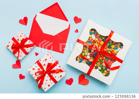 Red envelope with candy and gift box and Valentines hearts on colored background. Flat lay, top view. Romantic love letter for Holiday concept 125098136