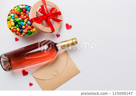Bottle of red wine on colored background for Valentine Day with gift and chocolate. Heart shaped with gift box of chocolates top view with copy space Bottle of red wine on colored background for Valentine Day with gift and chocolate. Heart shaped with gift box of chocolates top view with copy space 125098147