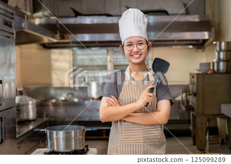 Confident Young Female Chef Holding Spatula in Commercial Kitchen 125099289
