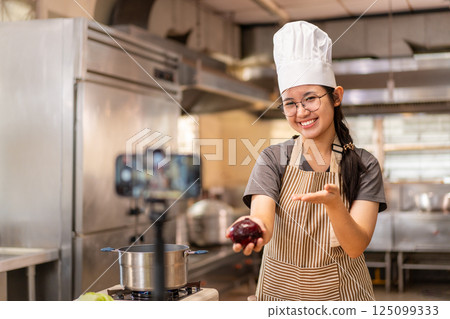 Smiling Female Chef Recording Cooking Video in Kitchen Smiling Female Chef Recording Cooking Video in Kitchen 125099333