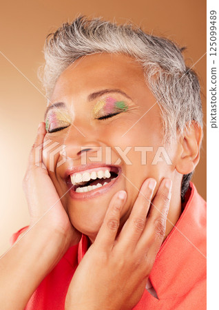 Happy, color and senior woman with makeup standing in a studio with colorful, trendy and edgy cosmetics. Happiness, smile and elderly lady with a beauty routine isolated by gradient brown background. 125099489