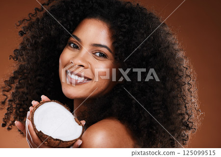 Beauty, coconut and woman skincare or hair care with happy smile or curls for natural oil and brown studio background. Portrait, African American model and happiness with fruit and afro product 125099515
