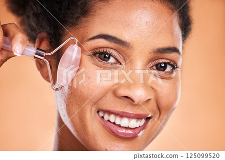 Massage, smile and black woman with a jade roller for facial health, wellness and beauty against orange studio background. Spa, skincare and face portrait of a model with a product for healthy skin Massage, smile and black woman with a jade roller for facial health, wellness and beauty against orange studio background. Spa, skincare and face portrait of a model with a product for healthy skin 125099520