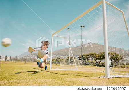 Soccer, sports and children with a goalkeeper saving a shot during a competitive game on a grass pitch or field. Football, kids and goal with a male child diving to save or stop a ball from scoring 125099697