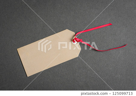 Gift tag with red ribbon on top of gray surface. Gift tag with red ribbon on top of gray surface. 125099713