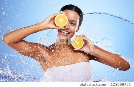 Woman, beauty and fruit with water splash in skincare hydration against blue studio background. Portrait of female holding orange in natural health or organic facial for vitamin C nutrition treatment 125099735