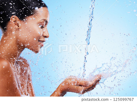 Water, splash and black woman doing skincare for health, wellness and hygiene in a studio. Beauty, shower and girl model doing a natural treatment for skin, body or face with aqua by blue background. 125099767