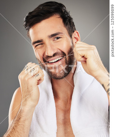 Floss, teeth and portrait of a man in studio cleaning his mouth with a dental wellness routine. Healthcare, dentistry and model flossing for oral care, health and hygiene isolated by gray background. Floss, teeth and portrait of a man in studio cleaning his mouth with a dental wellness routine. Healthcare, dentistry and model flossing for oral care, health and hygiene isolated by gray background. 125099899