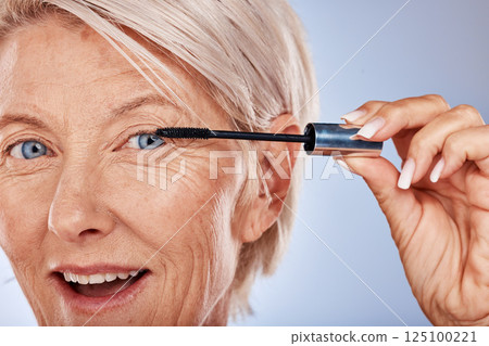Makeup, wow and senior woman with mascara for beauty, cosmetics and care for eyelash against a grey studio background. Happy, portrait and face of elderly cosmetic model with a product for a makeover 125100221