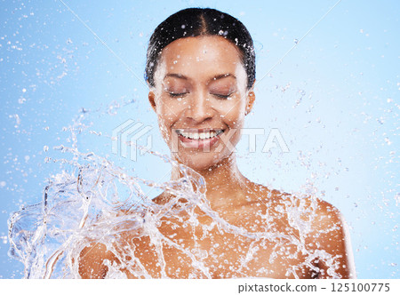 Water splash, shower and washing with a black woman in studio on a blue background for hygiene or hydration. Bathroom, happy and cleanliness with a young female model washing his skin for fresh care 125100775