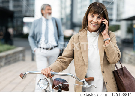 Phone call, bicycle and senior woman cycling to work while talking, speaking and in 5g conversation with business contact. Eco friendly transportation, communication and city person walking with bike Phone call, bicycle and senior woman cycling to work while talking, speaking and in 5g conversation with business contact. Eco friendly transportation, communication and city person walking with bike 125100814