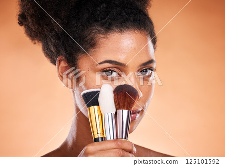 Makeup, brushes and portrait of a black woman in a studio doing a beautiful, natural and cosmetic routine. Cosmetics, beauty and young female model with facial products isolated by orange background. 125101592