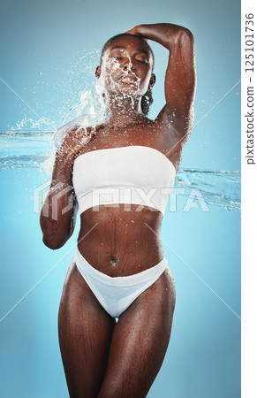Black woman, underwear and body with water splash on blue background in studio for skincare wellness, luxury healthcare or grooming. Beauty model, wet liquid or hydration spray for hygiene cleaning 125101736